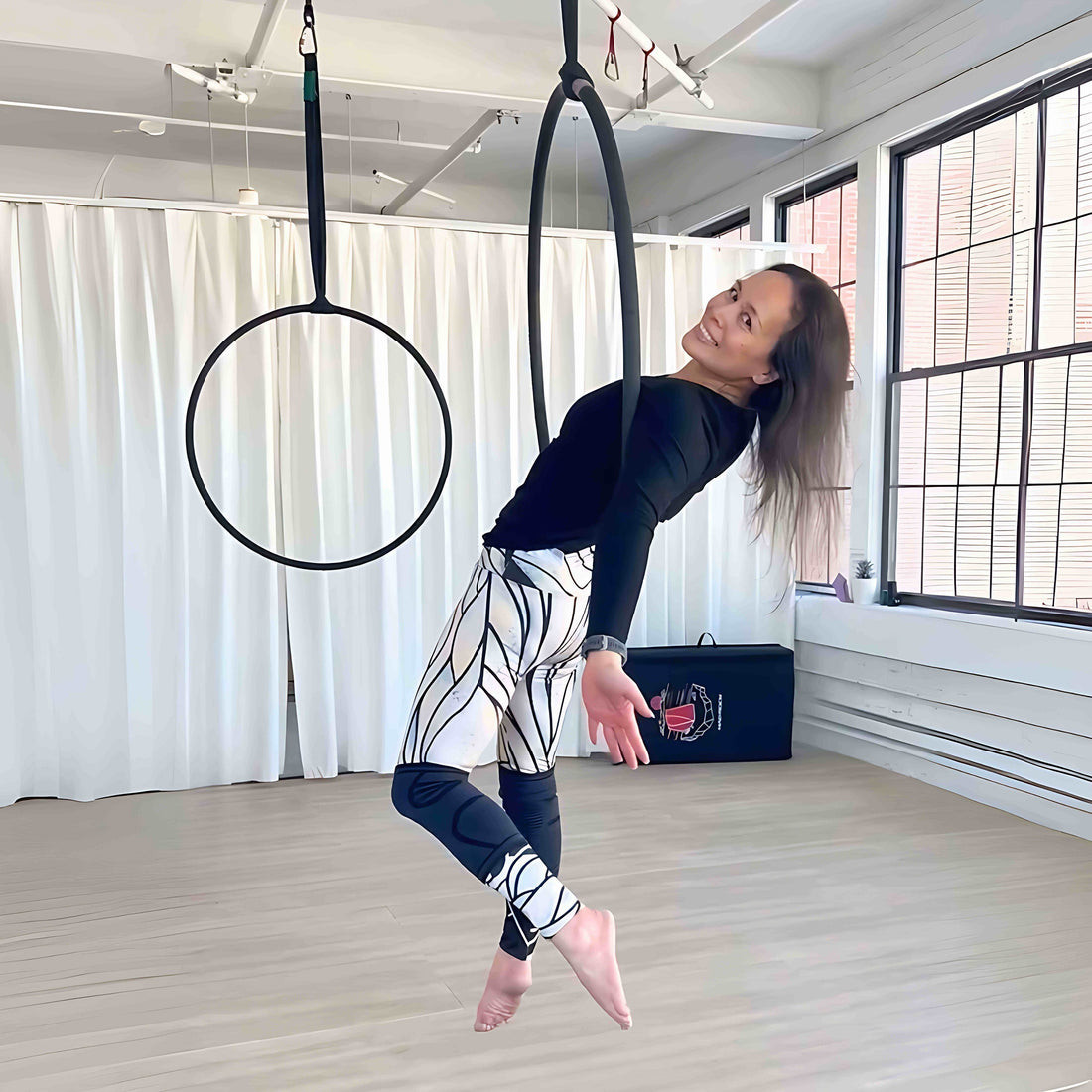 Det Agustin smiling mid-pose in an aerial hoop at a bright studio, wearing hand-drawn Umindak leggings and a black top. Capturing strength, expression, and creative freedom through movement.