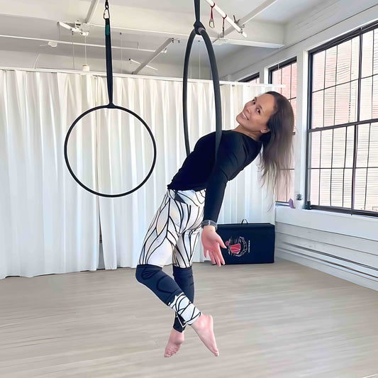 Det Agustin smiling mid-pose in an aerial hoop at a bright studio, wearing hand-drawn Umindak leggings and a black top. Capturing strength, expression, and creative freedom through movement.